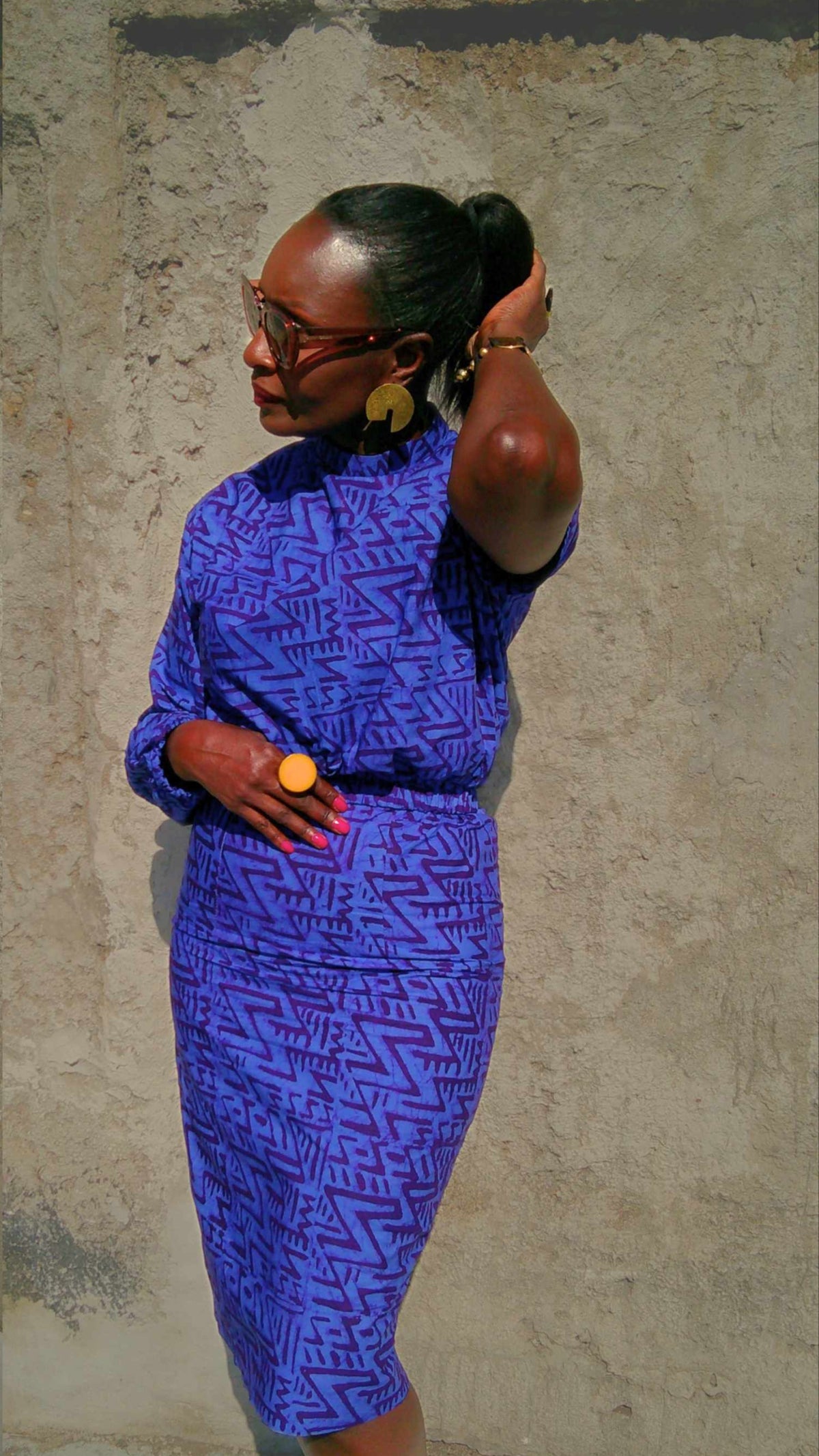 Woman in a blue patterned dress standing against a textured wall.