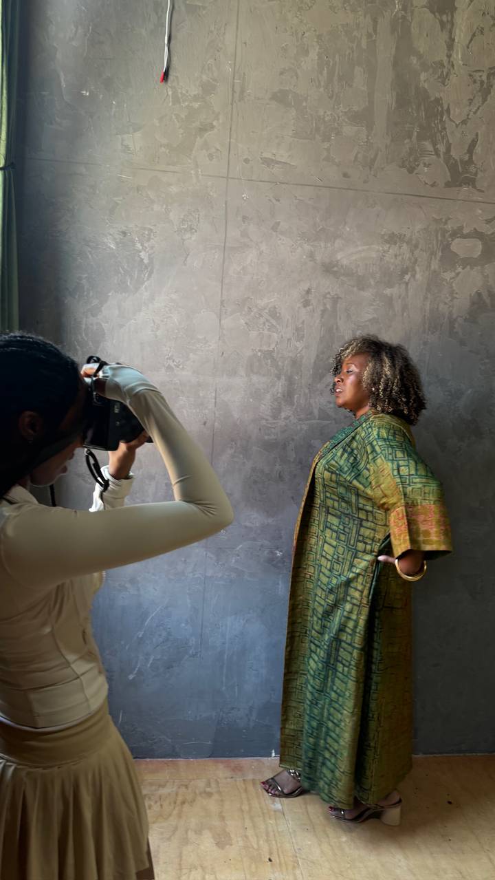 Behind the scenes on a LOVE DOT shoot — a photographer framing a woman in a hand-dyed green robe against a concrete wall.